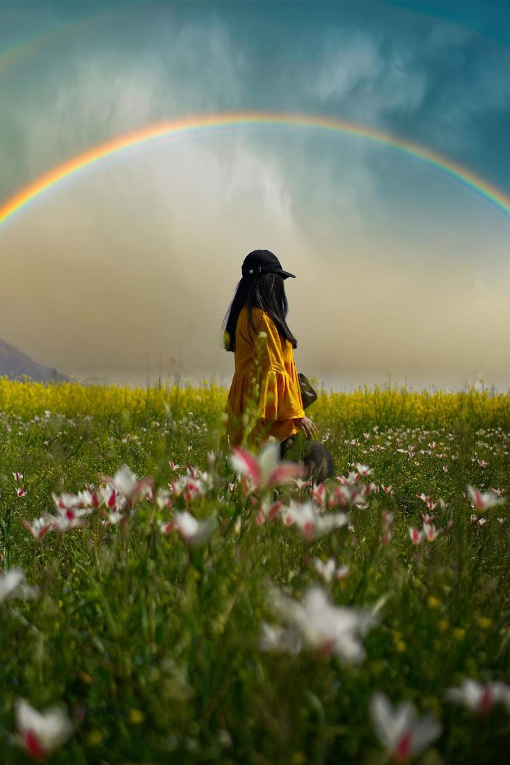 Solo traveller in a Kashmir meadow under a rainbow